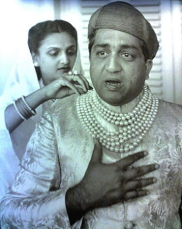 Maharajah Pratapsingh Rao Gaekwad wearing the Baroda pearl necklace. Maharani Sita Devi is in the background making adjustments to her husband's necklace